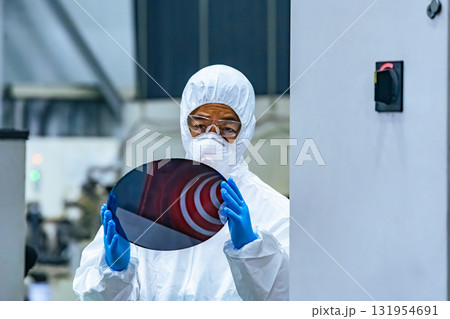 半導体工場でシリコンウエハーを検査する防護服を着た女性作業員 半導体工場でシリコンウエハーを検査する防護服を着た女性作業員 131954691