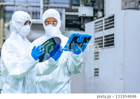 半導体工場でタブレットを持ってシリコンウエハーを検査する防護服を着た男女作業員 131954696