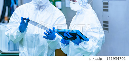 半導体工場でタブレットを持ってシリコンウエハーを検査する防護服を着た男女作業員 半導体工場でタブレットを持ってシリコンウエハーを検査する防護服を着た男女作業員 131954701