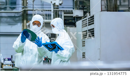 半導体工場でタブレットを見ながらシリコンウエハーを検査する防護服を着た男女作業員 131954775