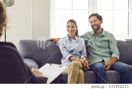 Young smiling couple sitting on sofa and talking with psychologist on therapy session. Young smiling couple sitting on sofa and talking with psychologist on therapy session. 131958213