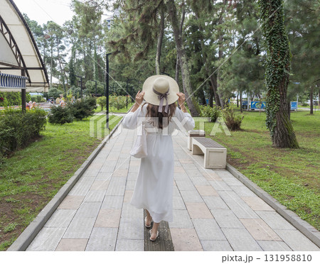 Attractive woman wearing creamy, off white outfit, straw hat in the park for a walk 131958810