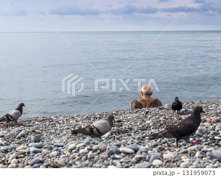 Very hairy senior man sitting at the beach surrounded by pigeons 131959073