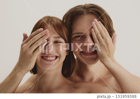 Happy couple covering one eye playfully symbolizing joyful self-expression Happy couple covering one eye playfully symbolizing joyful self-expression 131959388