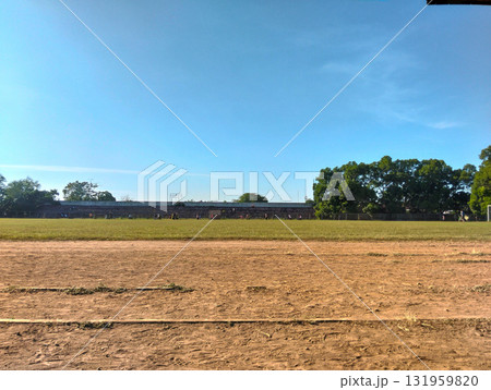 Wide outdoor athletic field with grassy pitch and dirt track under a clear blue sky, inviting sports and recreation. Wide outdoor athletic field with grassy pitch and dirt track under a clear blue sky, inviting sports and recreation. 131959820
