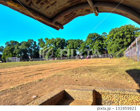 Vibrant sunny day at community sports field with distant soccer game and lush green trees under clear blue sky Vibrant sunny day at community sports field with distant soccer game and lush green trees under clear blue sky 131959821