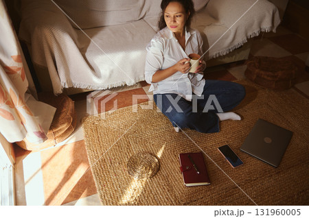 Cozy Morning At Home: Woman Sits On Rug With Coffee, Laptop, And Phone Cozy Morning At Home: Woman Sits On Rug With Coffee, Laptop, And Phone 131960005