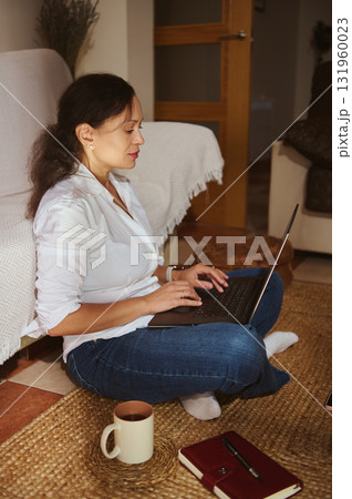 Woman Working From Home With Laptop, Cup Of Coffee, And Notebook In Cozy Living Room 131960023