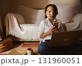 Woman Working From Home With Laptop And Phone, Relaxed Smile In Cozy Living Room Setting 131960051