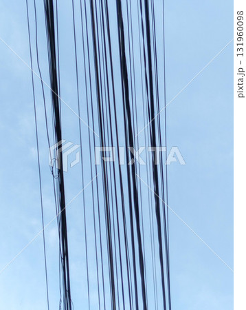 Intricate network of dark electrical wires creates a striking abstract pattern against a clear, pale blue sky, evoking urban infrastructure. 131960098