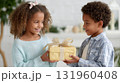 Smiling african children exchanging gift indoors in bright setting. 131960408