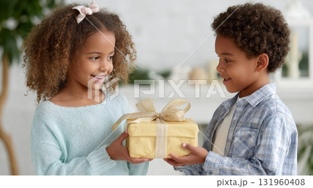 Smiling african children exchanging gift indoors in bright setting. 131960408