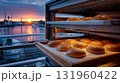 Warm golden buns in bakery oven with vibrant sunset over river. 131960422