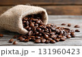 Burlap sack of roasted coffee beans spilling onto rustic wooden table. 131960423