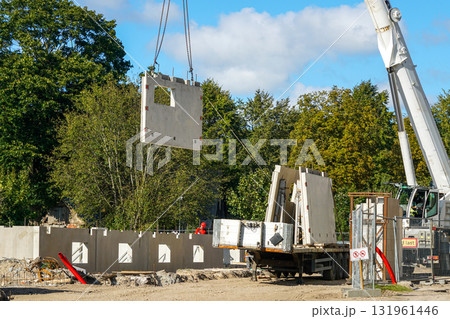 Crane lifting precast concrete wall panel at building site with workers and construction equipment Crane lifting precast concrete wall panel at building site with workers and construction equipment 131961446