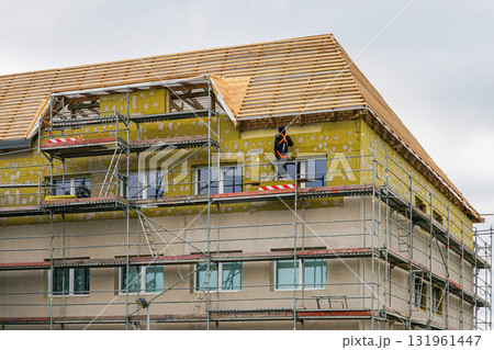 House renovation with facade insulation and scaffolding, worker installing thermal insulation 131961447