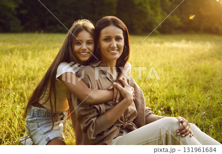 Smiling young mother with daughter sitting in the field on green grass and looking at camera. Smiling young mother with daughter sitting in the field on green grass and looking at camera. 131961684