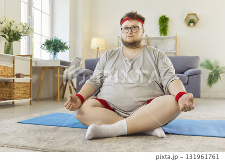 Yoga meditation of overweight man with big tummy at home, funny guy sitting on mat Yoga meditation of overweight man with big tummy at home, funny guy sitting on mat 131961761