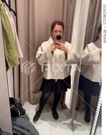 Trying on a cream jacket in a fitting room. Exploration of personal style, body confidence, and fashion self-expression through casual minimalism and neutral tones. 131961913