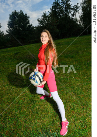 Young Woman in Sporty Outfit Holding Soccer Ball on a Grassy Field 131962289