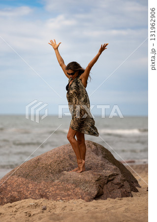 A joyful woman with arms wide on a rock by the serene beach embodies true freedom and happiness in nature A joyful woman with arms wide on a rock by the serene beach embodies true freedom and happiness in nature 131962906