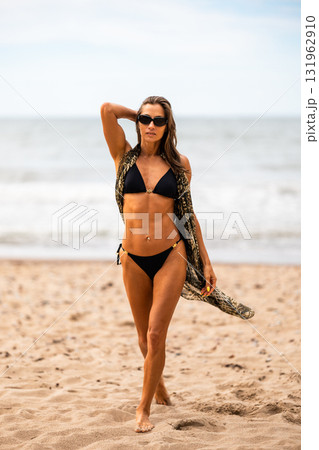 A confident woman struts gracefully along the sandy beach, showcasing vibrant summer fashion under the sunny day vibe A confident woman struts gracefully along the sandy beach, showcasing vibrant summer fashion under the sunny day vibe 131962910