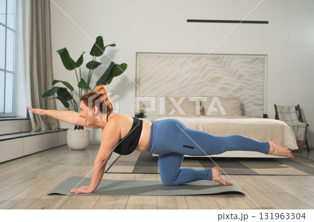 Yoga fitness workout training. Woman practicing yoga at home. Plus size female doing sports exercise on yoga mat indoor. Girl in sportswear have training workout for weight loss. Sport and fitness 131963304