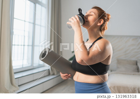 Yoga fitness sport workout training. Woman holding yoga mat drinking bottle water ready for practicing yoga fitness at home. Plus size girl in sportswear have training workout for weight loss indoor 131963318