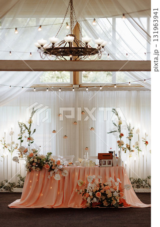 Elegant wedding sweetheart table with peach drapery and floral decorations in bright hall 131963941