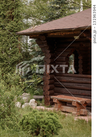 Wooden log gazebo with bench surrounded by green trees and grass in summer garden Wooden log gazebo with bench surrounded by green trees and grass in summer garden 131963944