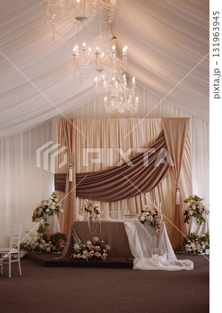 Elegant wedding ceremony stage with beige drapery and chandeliers in decorated hall 131963945