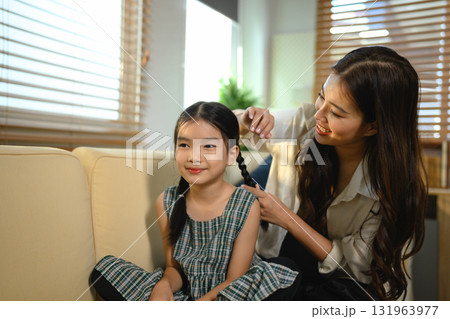 The mother is lovingly styling her daughter's hair The girl is sitting on a couch and smiling, Scene is happy and friendly The mother is lovingly styling her daughter's hair The girl is sitting on a couch and smiling, Scene is happy and friendly 131963977