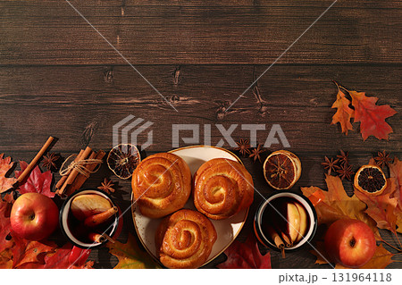 Cinnamon rolls with hot autumn drink, mulled wine with apples and autumn fallen leaves, star anise, ginger and cinnamon on wooden table, banner for display, autumn greeting concept, mockup for menu. Cinnamon rolls with hot autumn drink, mulled wine with apples and autumn fallen leaves, star anise, ginger and cinnamon on wooden table, banner for display, autumn greeting concept, mockup for menu. 131964118
