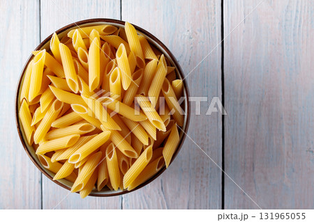 Dry Yellow Penne Pasta in Bowl on Wooden Background Top View Copy Space Dry Yellow Penne Pasta in Bowl on Wooden Background Top View Copy Space 131965055