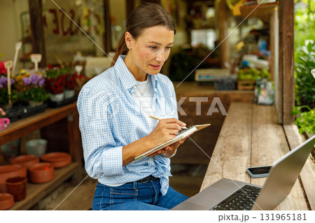 A Young Woman is Engaged in Working on Her Laptop in a Cozy Plant Shop Environment 131965181