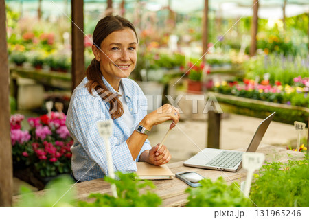 A Happy Woman is Working Enthusiastically in a Colorful Flower Shop with Her Laptop 131965246