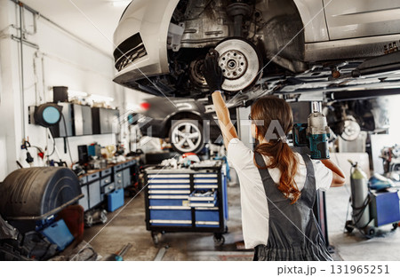 An Automotive Mechanic is diligently working on a car using a lift in the garage environment An Automotive Mechanic is diligently working on a car using a lift in the garage environment 131965251