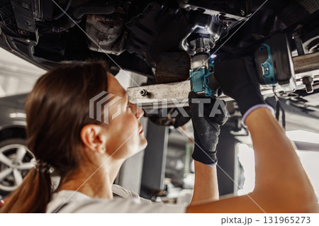 A Skilled Female Mechanic Hard at Work Beneath a Car, Utilizing Various Power Tools Effectively 131965273
