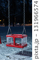 A vibrant red child's swing, completely encased in thick ice and sharp icicles, hangs quietly in a snowy park at dusk, illuminated by subtle ambient light. 131966574