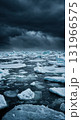 A powerful wide shot of countless ice floes and small icebergs floating on dark teal water beneath a dramatic, stormy, and heavily overcast sky, conveying a cold, remote environment. 131966575