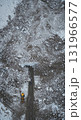 An aerial perspective captures a yellow snowplow on a winding road amidst a rugged, snow-dusted winter landscape featuring scattered white ice and dark rock formations. 131966577