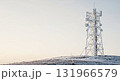 A towering telecommunications mast, covered in frost, stands on a snow-dusted hill under a bright, clear sky, symbolizing global connectivity and remote infrastructure. 131966579