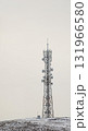 A tall cellular communication tower stands prominently on a snow-covered hill under a bright overcast sky, offering ample copy space. 131966580
