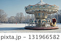 A vintage carousel with white horses and icicles stands silently in a snow-covered park under a clear blue sky, evoking a serene winter wonderland. 131966582