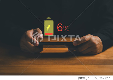 Close-up of hands holding smartphone with digital battery warning icon showing 6% low power, symbolizing charging, energy consumption, battery drain, mobile device, power saving and technology. 131967767