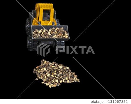 A creative and unique macro studio shot of a miniature yellow and grey plastic toy construction front loader, isolated against a dramatic black background, scooping a mound of whole black peppercorns. 131967822