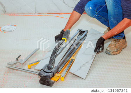 Construction worker carefully cuts ceramic tiles with tile cutter, preparing for installation. Construction worker carefully cuts ceramic tiles with tile cutter, preparing for installation. 131967841