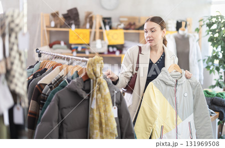 Adult woman chooses down jacket in clothing store Adult woman chooses down jacket in clothing store 131969508