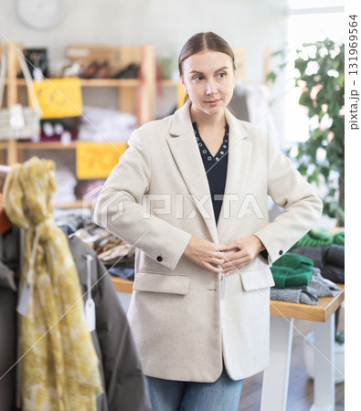 Glad young woman trying on winter coat in clothing store 131969564