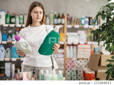 Young woman buyer chooses detergent in store Young woman buyer chooses detergent in store 131969653
